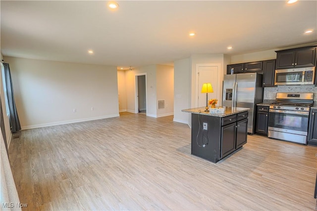 kitchen with a center island, stainless steel appliances, light stone counters, backsplash, and light wood-type flooring