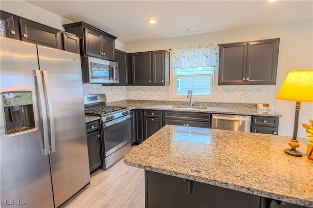 kitchen featuring backsplash, sink, light stone countertops, appliances with stainless steel finishes, and light hardwood / wood-style floors