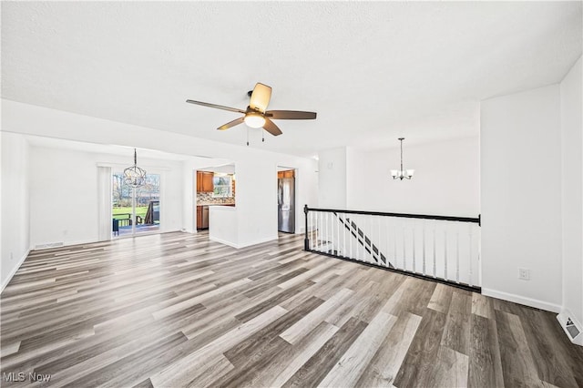 unfurnished living room with a textured ceiling, wood-type flooring, and ceiling fan with notable chandelier