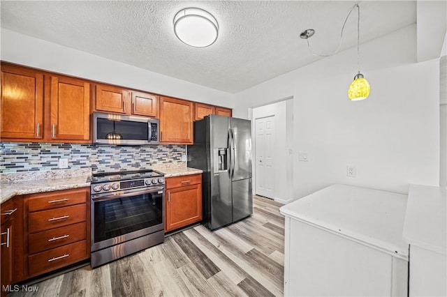 kitchen with appliances with stainless steel finishes, light wood-type flooring, backsplash, light stone counters, and pendant lighting