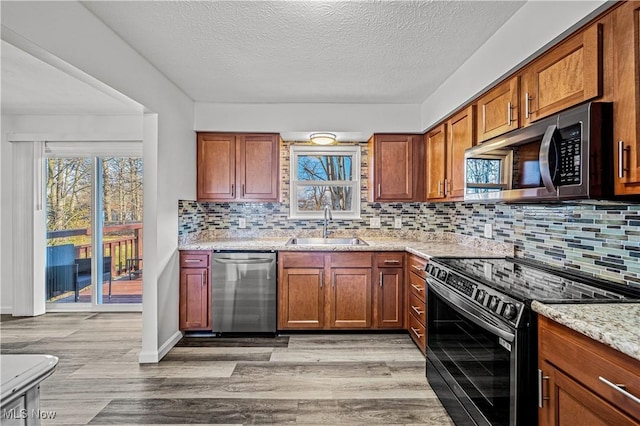 kitchen with sink, light stone countertops, tasteful backsplash, light hardwood / wood-style floors, and stainless steel appliances