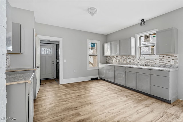 kitchen with decorative backsplash, light wood-type flooring, gray cabinetry, and sink