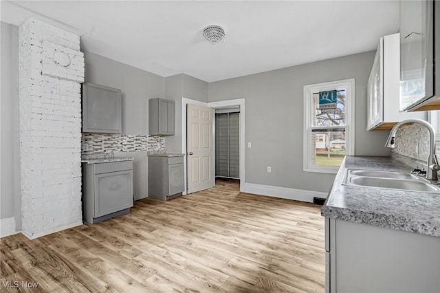 kitchen with decorative backsplash, light wood-type flooring, gray cabinetry, and sink