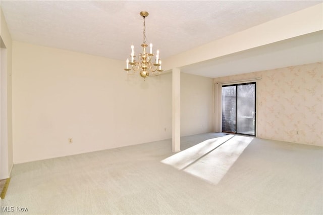 carpeted empty room featuring a textured ceiling and a chandelier