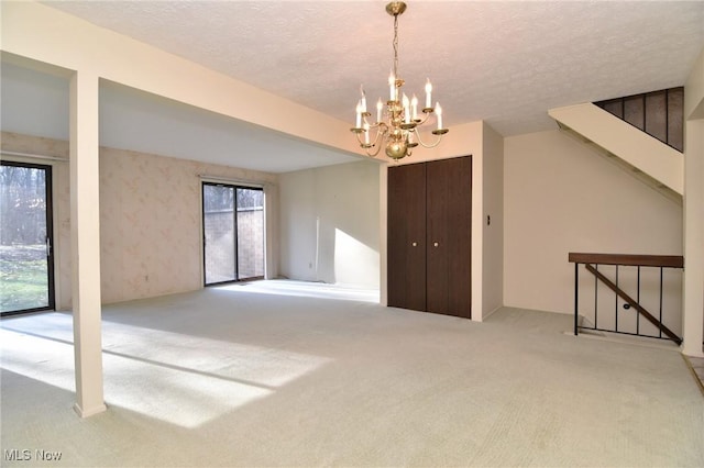 empty room featuring light colored carpet, a textured ceiling, and an inviting chandelier