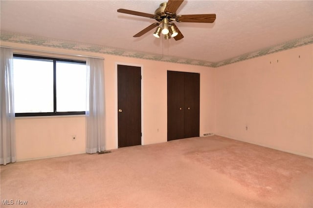 unfurnished bedroom featuring a textured ceiling, ceiling fan, light carpet, and multiple closets