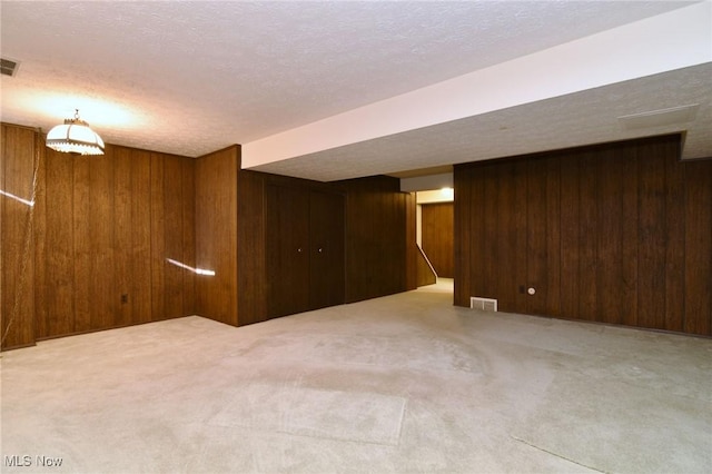 basement featuring wooden walls, light colored carpet, and a textured ceiling