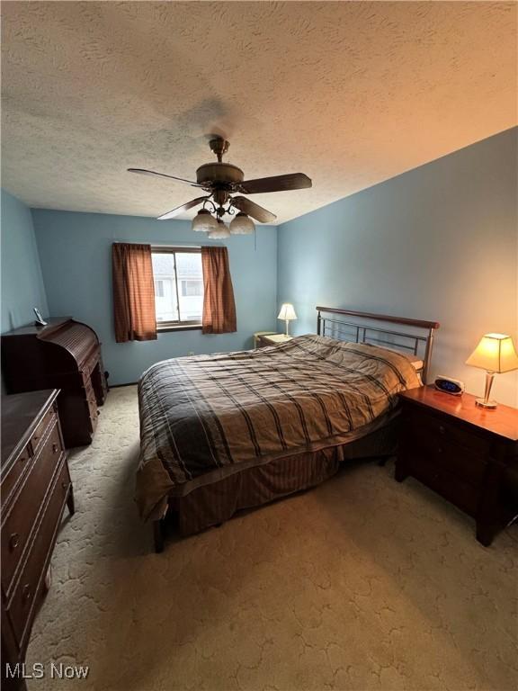 carpeted bedroom with ceiling fan and a textured ceiling