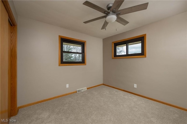 carpeted empty room with ceiling fan and plenty of natural light