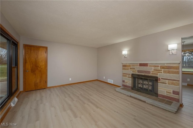 unfurnished living room with a textured ceiling, light hardwood / wood-style floors, and a stone fireplace