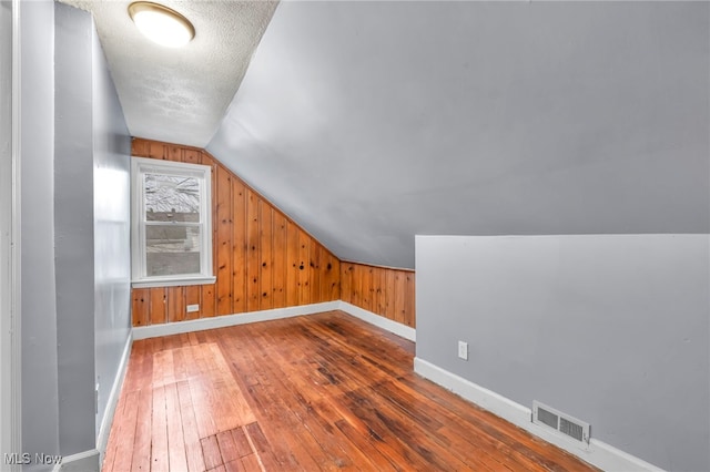 additional living space featuring a textured ceiling, wood walls, lofted ceiling, and hardwood / wood-style flooring