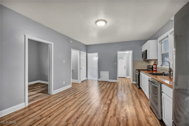 kitchen featuring sink, tasteful backsplash, appliances with stainless steel finishes, white cabinets, and light wood-type flooring