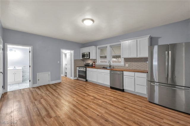 kitchen with sink, stainless steel appliances, wood counters, white cabinets, and light wood-type flooring