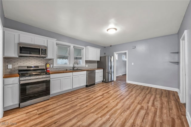 kitchen with appliances with stainless steel finishes, backsplash, a wealth of natural light, light hardwood / wood-style flooring, and white cabinetry