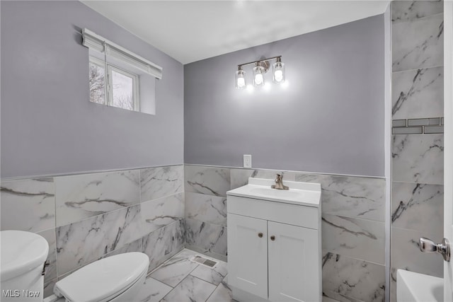 bathroom with a bathing tub, vanity, tile walls, and toilet