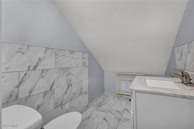 bathroom with vanity, lofted ceiling, toilet, a textured ceiling, and tile walls