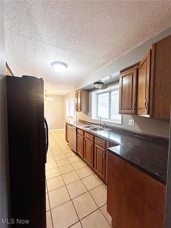 kitchen with a textured ceiling, black refrigerator, light tile patterned floors, and sink