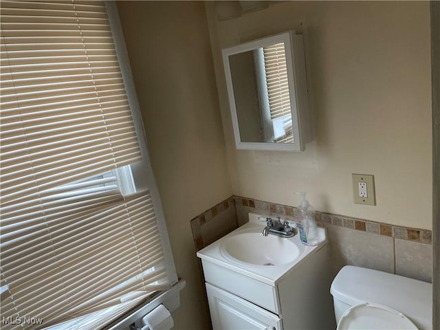 bathroom with tile walls, a wainscoted wall, vanity, and toilet