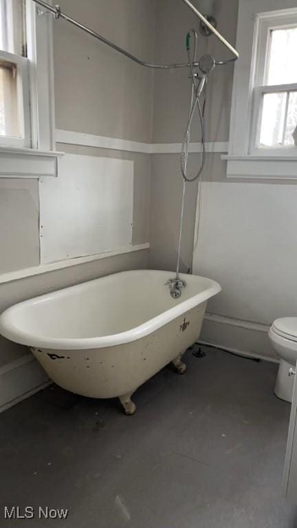 bathroom featuring concrete floors, a tub to relax in, and toilet