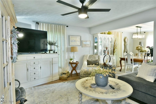 living room with ceiling fan, a textured ceiling, and light wood-type flooring