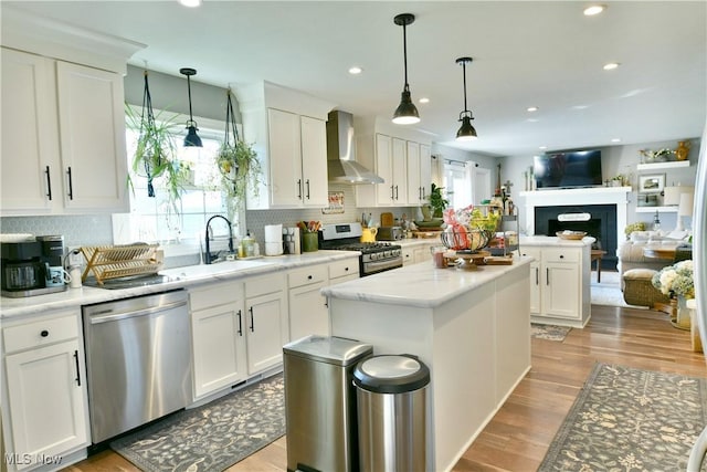 kitchen with white cabinets, pendant lighting, stainless steel appliances, and wall chimney exhaust hood