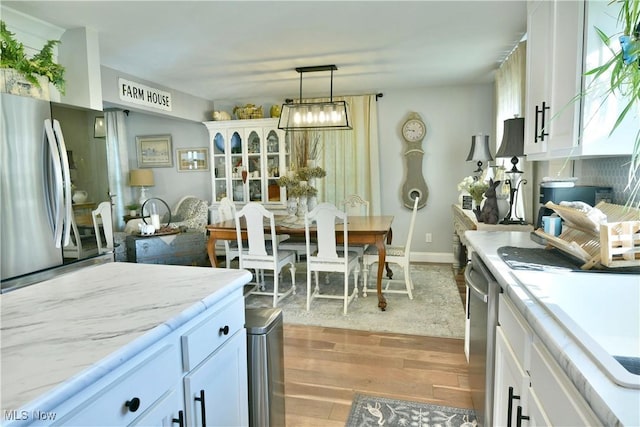 kitchen with hanging light fixtures, white cabinets, light wood-type flooring, and appliances with stainless steel finishes