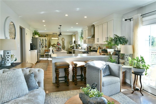 kitchen with pendant lighting, a breakfast bar, wall chimney range hood, light hardwood / wood-style flooring, and kitchen peninsula