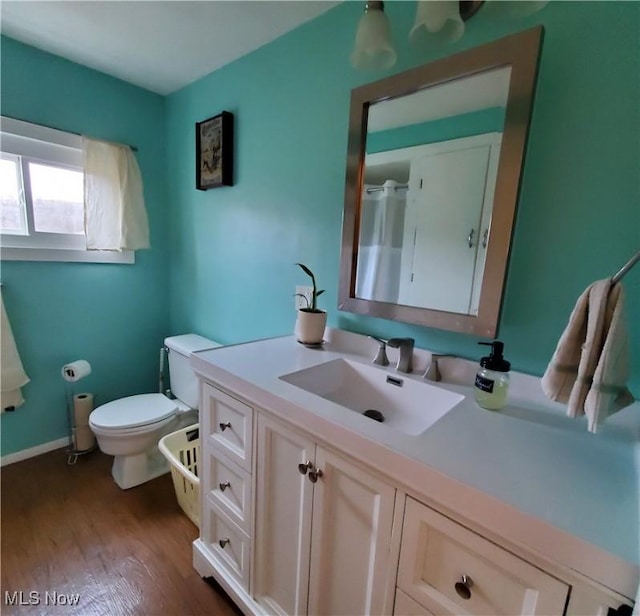 bathroom featuring vanity, baseboards, wood finished floors, and toilet