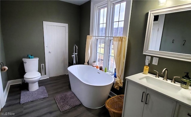 bathroom with a freestanding bath, toilet, wood finished floors, and a wealth of natural light