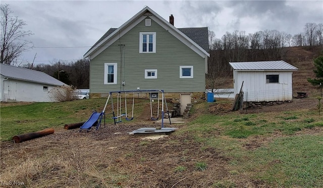 rear view of house featuring a playground, a chimney, and a lawn