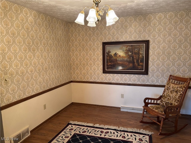 unfurnished room with baseboard heating, a notable chandelier, a textured ceiling, and hardwood / wood-style flooring