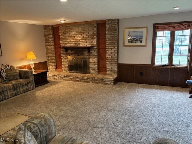 carpeted living room featuring a textured ceiling, wood walls, and a fireplace