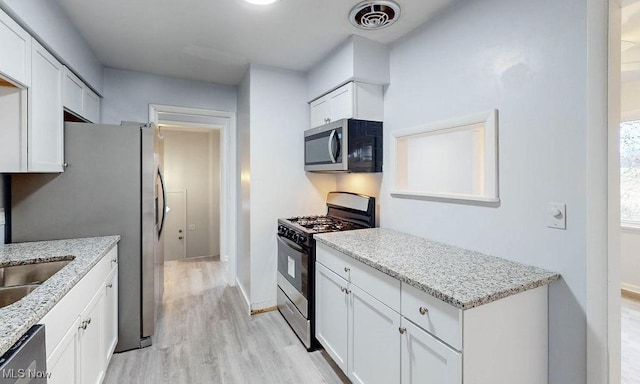 kitchen featuring white cabinetry, sink, stainless steel appliances, light stone counters, and light hardwood / wood-style floors