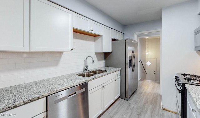 kitchen with light stone countertops, white cabinetry, sink, light hardwood / wood-style floors, and appliances with stainless steel finishes