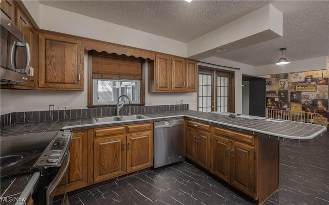 kitchen with kitchen peninsula, a textured ceiling, stainless steel appliances, sink, and tile countertops