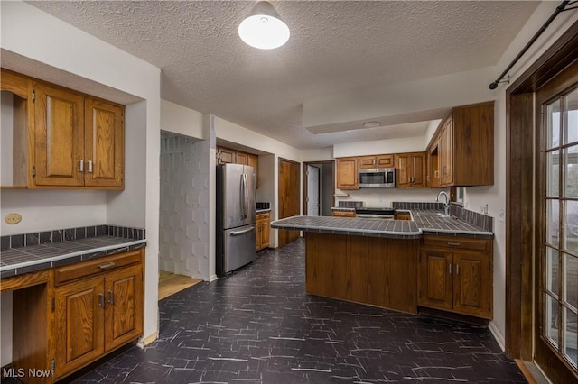 kitchen featuring sink, tile counters, a textured ceiling, and appliances with stainless steel finishes