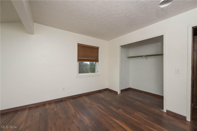 unfurnished bedroom with dark hardwood / wood-style floors, beam ceiling, a textured ceiling, and a closet