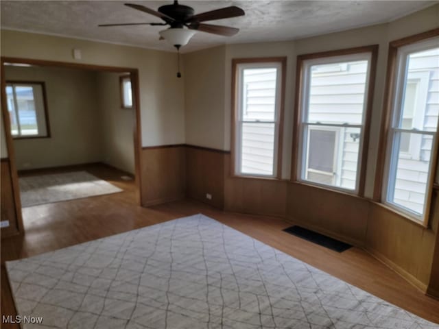 spare room featuring ceiling fan, light hardwood / wood-style floors, and wooden walls