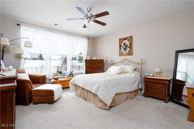 bedroom with ceiling fan, light colored carpet, and a textured ceiling