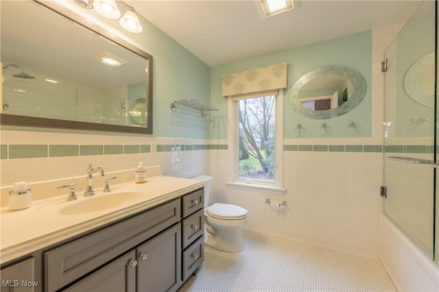 full bathroom featuring tile patterned floors, bath / shower combo with glass door, toilet, vanity, and tile walls