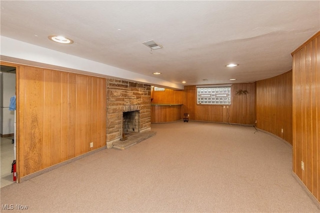 unfurnished living room featuring wooden walls, a fireplace, and light colored carpet