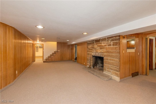 unfurnished living room featuring light carpet, a stone fireplace, and wooden walls