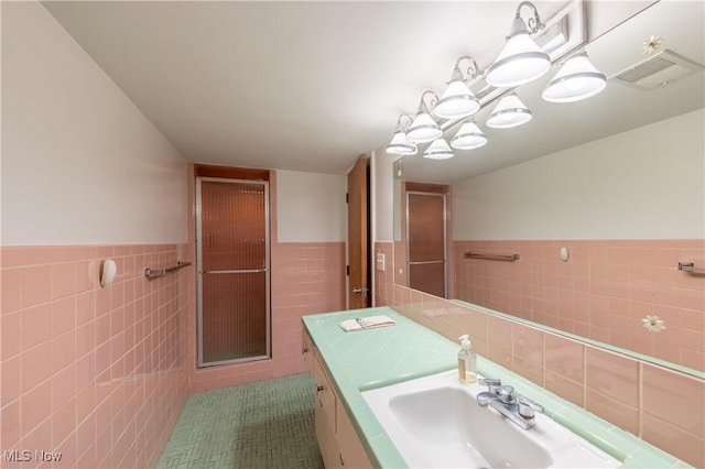 bathroom with tile patterned flooring, vanity, a shower with shower door, and tile walls