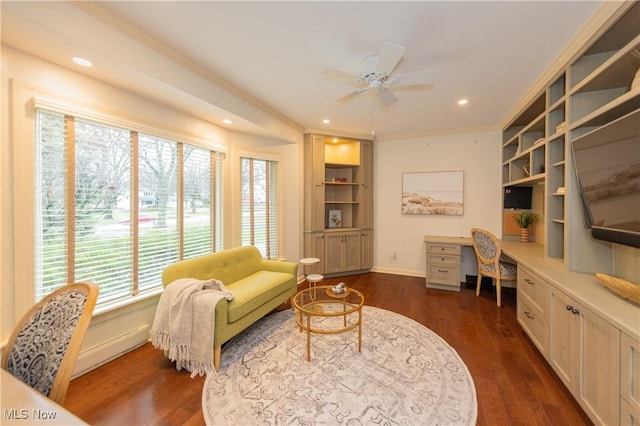 living area with plenty of natural light, dark hardwood / wood-style floors, built in desk, and ceiling fan