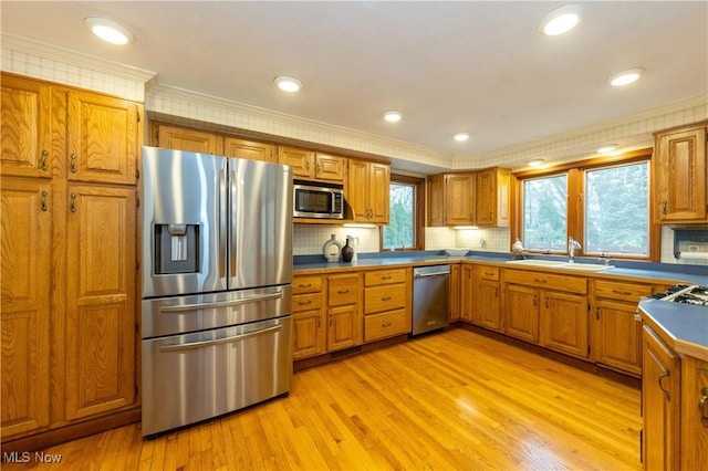 kitchen featuring appliances with stainless steel finishes, light hardwood / wood-style floors, crown molding, and sink