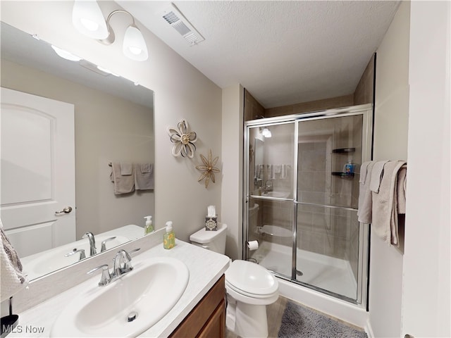 bathroom featuring a shower with door, vanity, a textured ceiling, and toilet