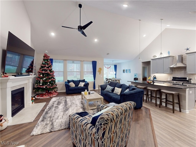 living room with high vaulted ceiling, light hardwood / wood-style flooring, ceiling fan, and sink