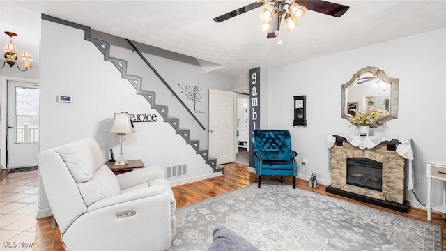 living room featuring ceiling fan, a stone fireplace, and wood-type flooring