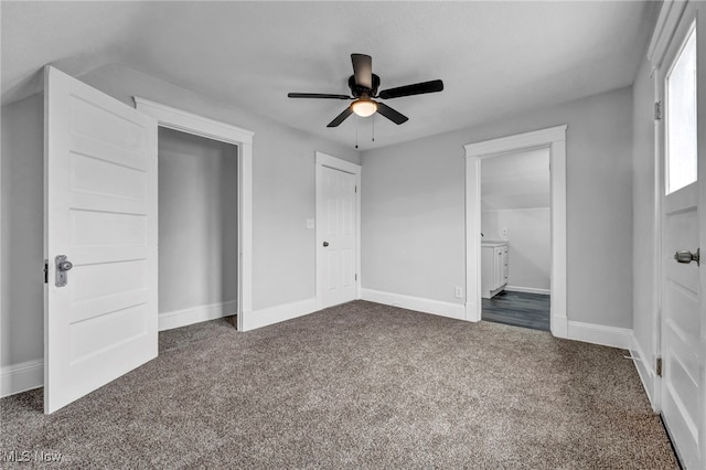 unfurnished bedroom featuring ceiling fan, dark carpet, ensuite bathroom, and a closet