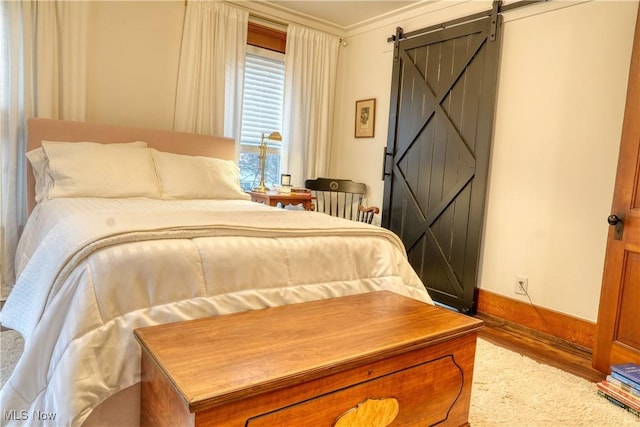 bedroom with a barn door, hardwood / wood-style flooring, and crown molding